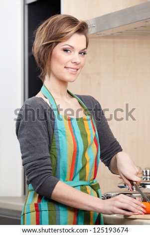 Young girl in striped apron cooks vegetables in the modern comfortable kitchen