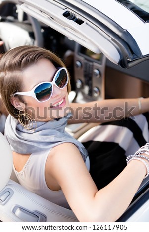 Pretty woman wearing sunglasses with white rim turns back sitting in the car