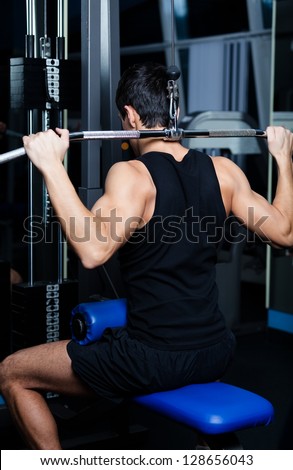 Athletic young man works out on training apparatus in gym class