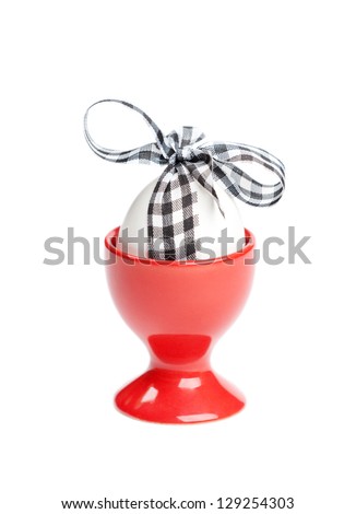 Easter egg with checked ribbon is in red egg cup, isolated on white. Traditional symbol of the feast