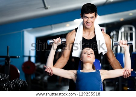 Coach helps woman to exercise with dumbbells in fitness gym