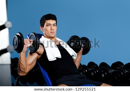 Bodybuilder exercises with weights in gym class against a set of dumbbells
