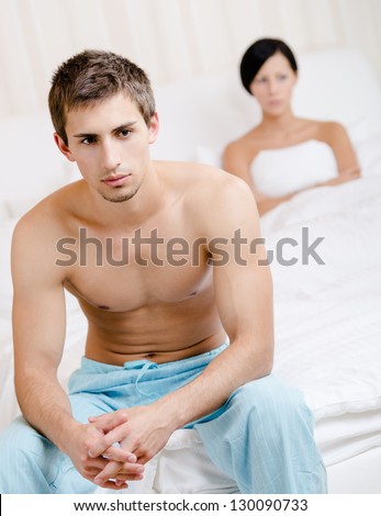 Young couple argues in bedroom. Depressed man sitting on the edge of the bed. Focus on man