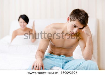 Young couple quarrels in bed. Depressed male sitting on the edge of the bed. Focus on man