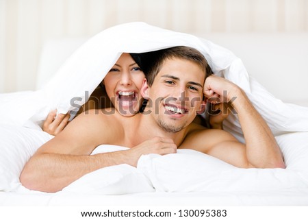Close up of couple playing in bed. Covered with blanket woman lying on the back of the man