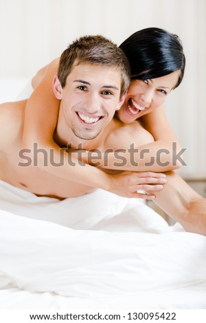 Close up of laughing couple who plays in bed-room. Woman lying on the back of the man embraces him
