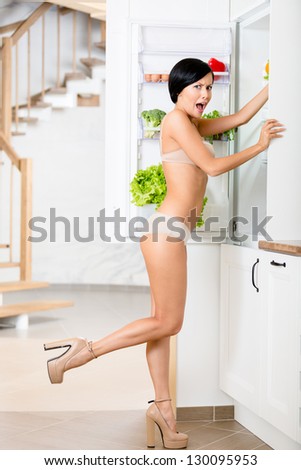 Full length of woman near the opened fridge full of vegetables and fruit. Concept of healthy and dieting food
