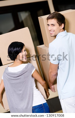 Back view of happy couple carrying cardboard boxes while moving to new house