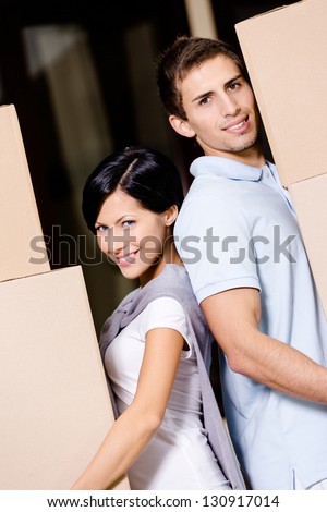 Happy couple stands back to back while carrying cardboard containers and moving to new house