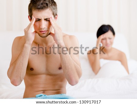 Young couple argues in bed. Depressed man sitting on the edge of the bed. Focus on man