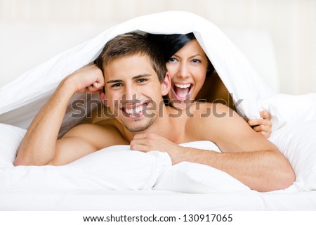 Close up of couple playing in bedroom. Covered with blanket woman lying on the back of the man