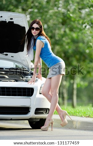 Woman repairing the broken car on the highway. Girl stands near opened hood of the car after an accident