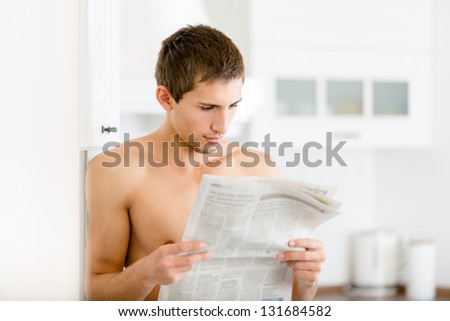 Naked man reads newspaper standing near the fridge at the kitchen
