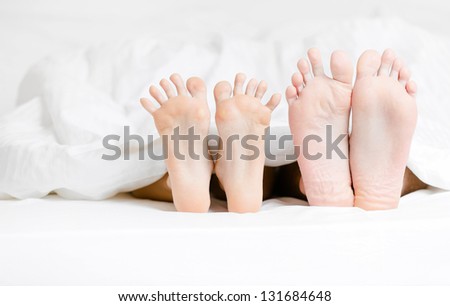 Close up view of two pairs of feet of the couple next to each other in bed