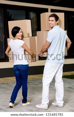 Back view of happy couple carrying cardboard containers while moving to new house