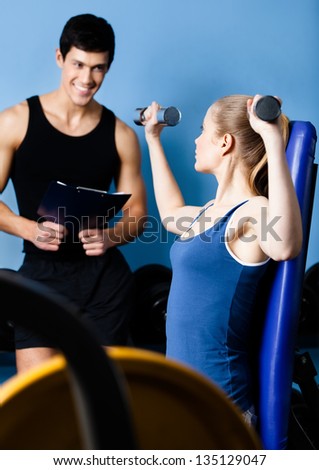 Coach controls sports actions of pretty woman working out with dumbbells in gym