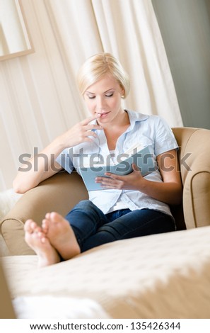 Lady sitting on the sofa reads a book. Concept of education and useful pastime