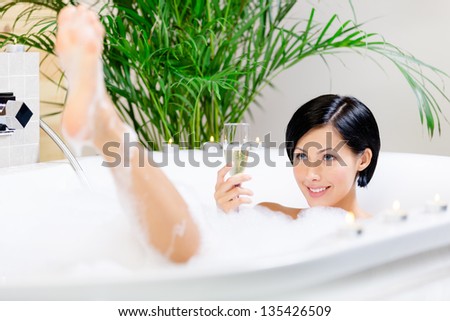 Woman taking a bath with suds drinks champagne