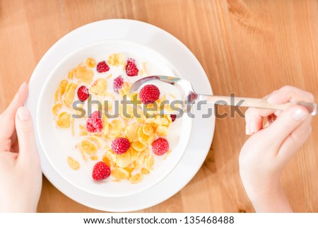Top view of hands of the woman eating cereals with strawberry and milk