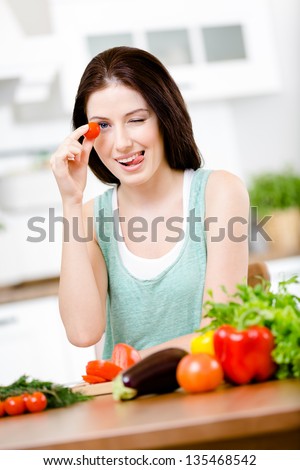 Woman keeps tomato sitting at the table with a great variety of groceries for salad