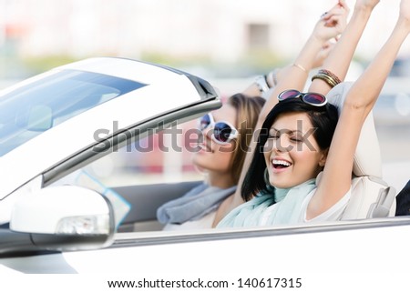 Female friends driving car with the hands up and having fun on the vacation