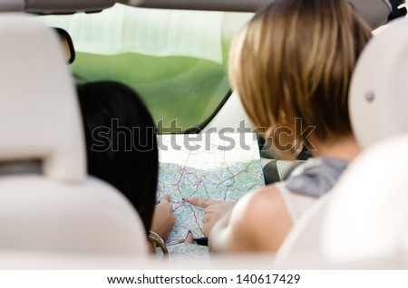 Back view of girls who lost their way and checking the way with the help of the highway map in the car