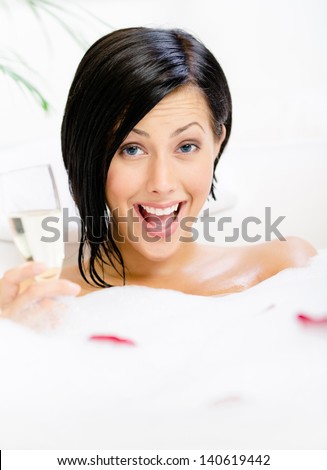 Woman taking a bath with suds and rose petals drinks alcohol and relaxes