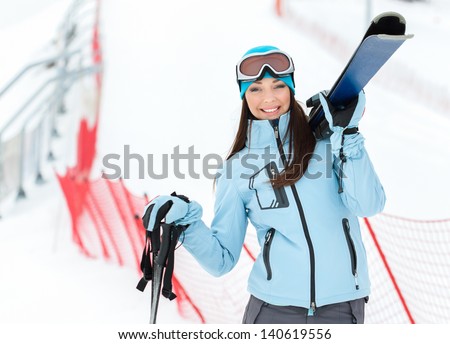 Half-length portrait of female wearing sports jacket and goggles who hands skis