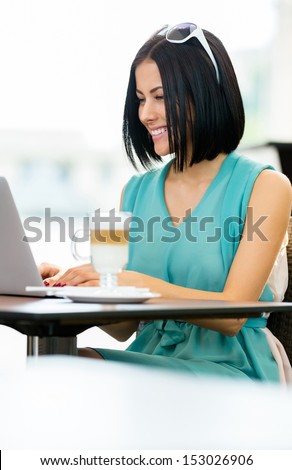 Girl wearing blue dress and sunglasses sits at the table of the bar and works at the computer