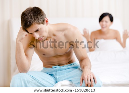 Young couple argues in bed. Depressed young man sitting on the edge of the bed. Focus on man