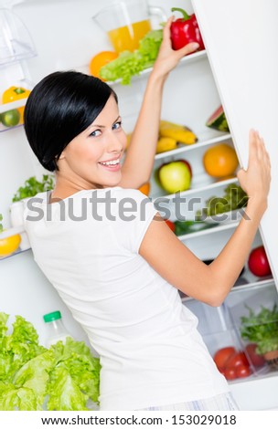 Woman takes bell pepper from the opened refrigerator full of vegetables and fruit. Concept of healthy and dieting food