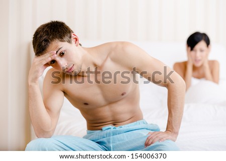 Young couple argues in bed. Depressed male sitting on the edge of the bed. Focus on man