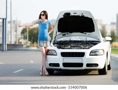 Woman hitchhiking near the opened hood of the broken car and waiting for assistance
