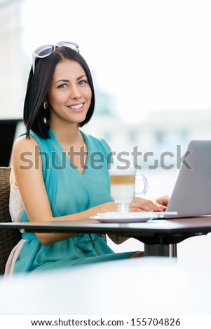 Girl wearing blue dress and sunglasses sits at the table of the cafe and works at the computer