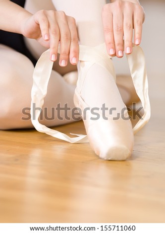 Close up view of legs of sitting on the floor ballerina who laces the ribbons of the pointes