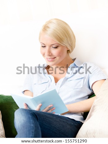 Lady sitting on the couch reads a book. Concept of education and useful pastime
