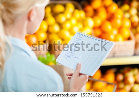 Girl looks through shopping list near the heap of fruits lying in the braided baskets in the shop