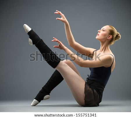 Sideview of dancing on the floor ballerina with her leg up, isolated on grey. Concept of elegant art and sportive hobby