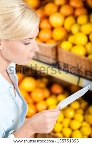 Girl looks through shopping list near the stack of fruits lying in the braided baskets in the market
