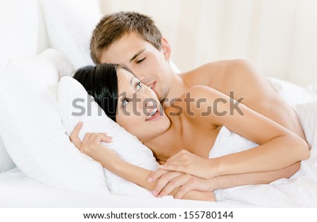 Man lying in bed with white linen embraces woman. Concept of love and affection