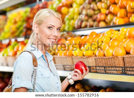 Girl at the shopping center choosing fruits and vegetables hands fresh red apple