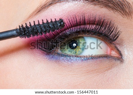 Close up of female eye with brilliant make-up and brush applying mascara on eyelashes