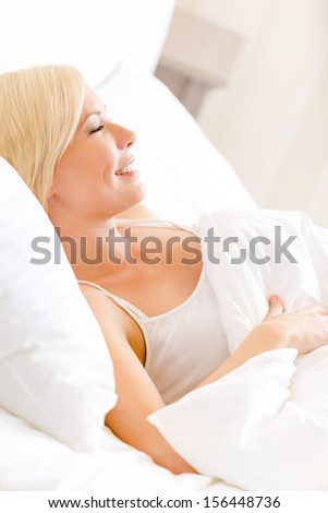 Smiley woman lying in bed under the warm blanket