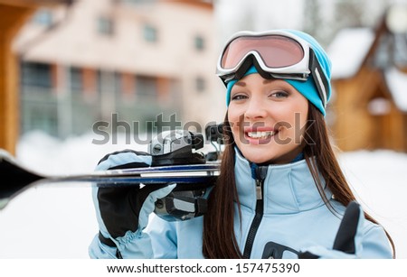 Close up of woman wearing sports jacket and goggles who hands skis and thumbs up