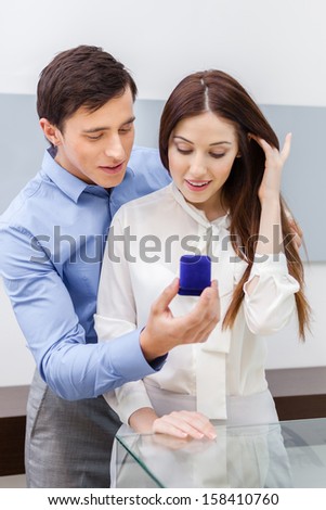 Young man presents engagement ring to his woman at jeweler\'s shop. Concept of wealth and luxurious life