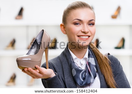 Portrait of woman keeping coffee-colored shoe in shopping center against the showcase with footwear
