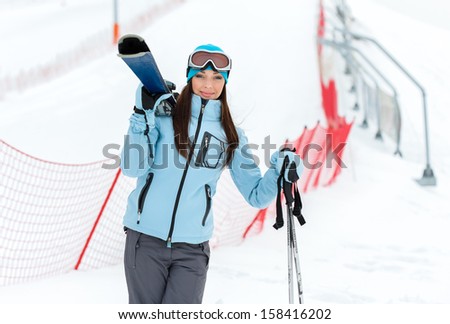 Half-length portrait of female wearing sports jacket and goggles who holds skis