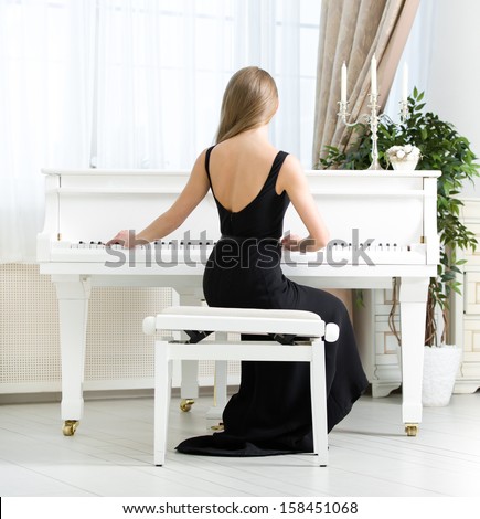 Back view of woman in black dress sitting and playing piano. Concept of music and arts