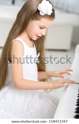 Portrait of little girl in white dress playing piano. Concept of music study and creative hobby