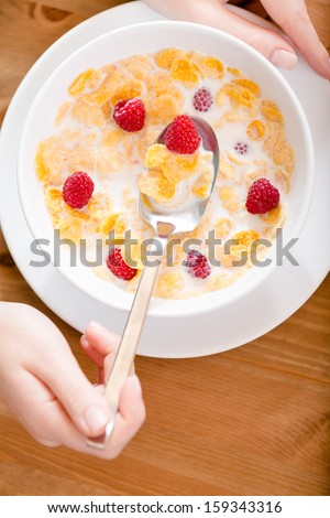Top view of plate with cereals, strawberry, milk and hand keeping a spoon